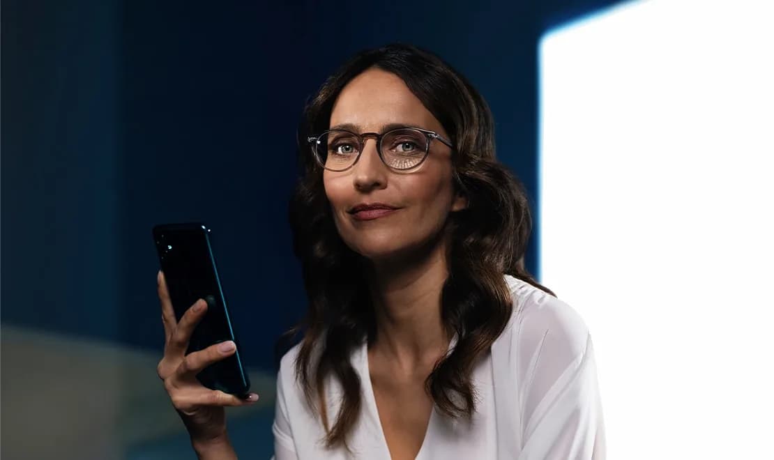 Essilor Varilux Physio extensee Transitions Gen S Lenses, official Essilor Varilux Physio extensee image of a woman in spectacles holding a smartphone